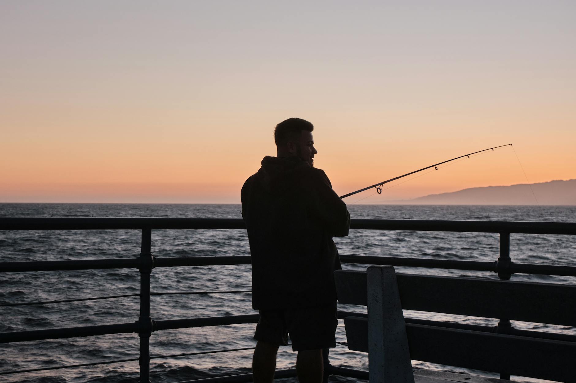 Fishing rod and reel silhouetted against a Miami ocean sunset