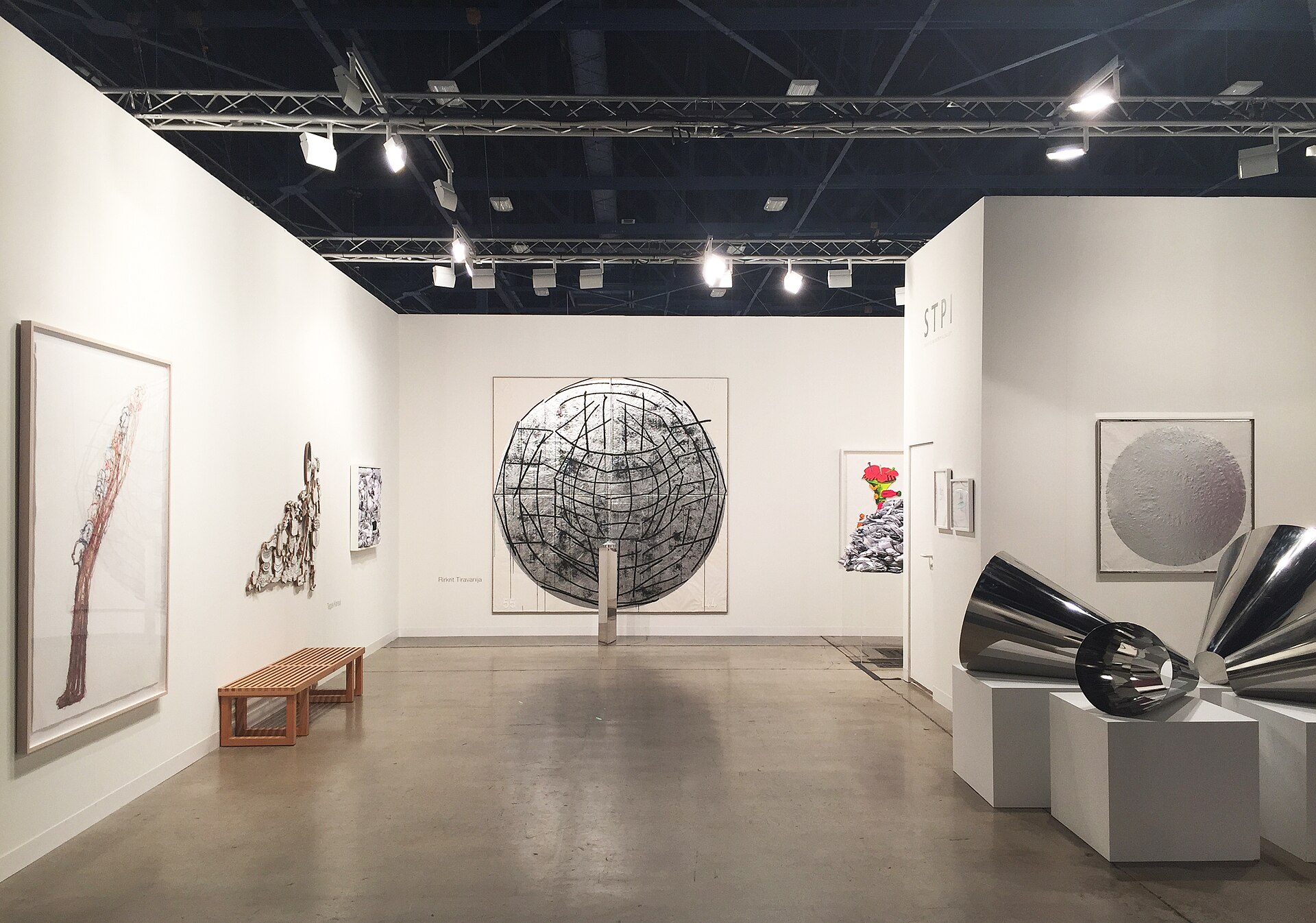 A gallery booth at Art Basel Miami Beach with large artworks on white walls and polished steel sculptures in the foreground