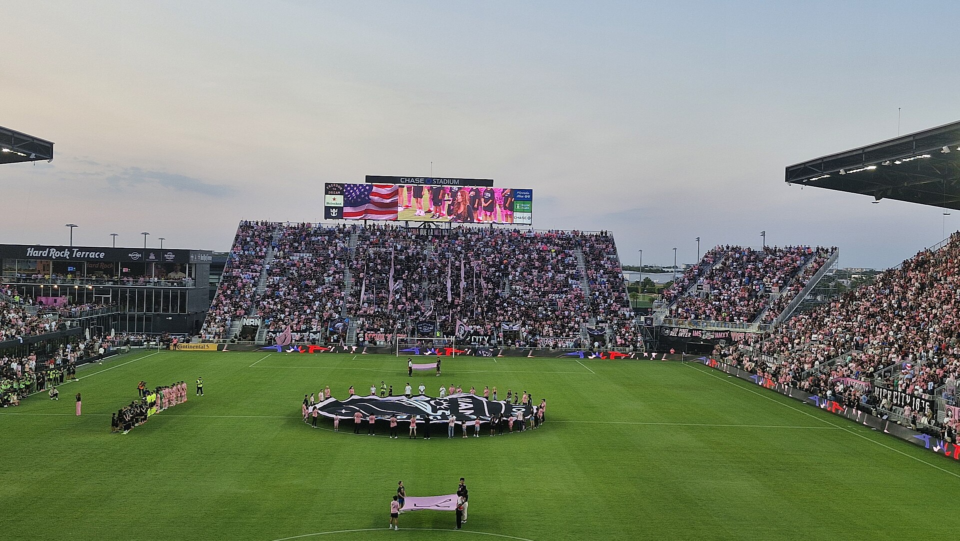 A full crowd at Chase Stadium in Fort Lauderdale during the pre-match ceremony for Inter Miami against Nashville SC, with a giant club crest flag on the field