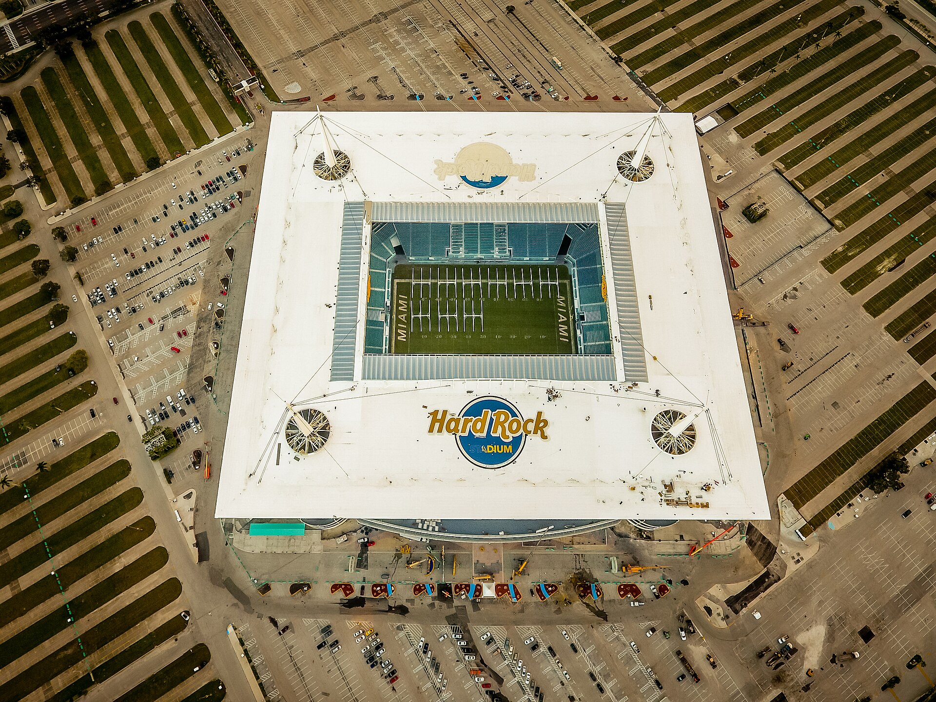 Aerial view of Hard Rock Stadium's square white canopy and the field inside, surrounded by rows of parking lots and palm-lined medians