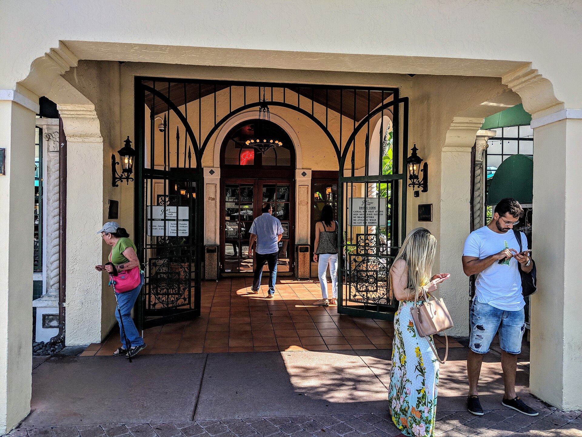 The arched entrance and wrought-iron gates of Joe's Stone Crab restaurant in Miami Beach, with a dress code sign by the door
