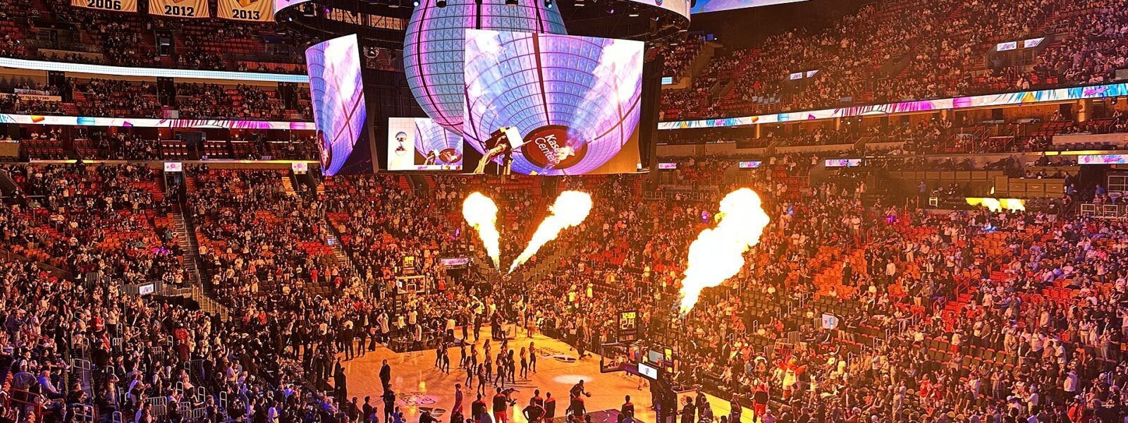 Flames shooting up beside the court during pre-game introductions at a packed Kaseya Center, with the 2006, 2012 and 2013 championship banners overhead