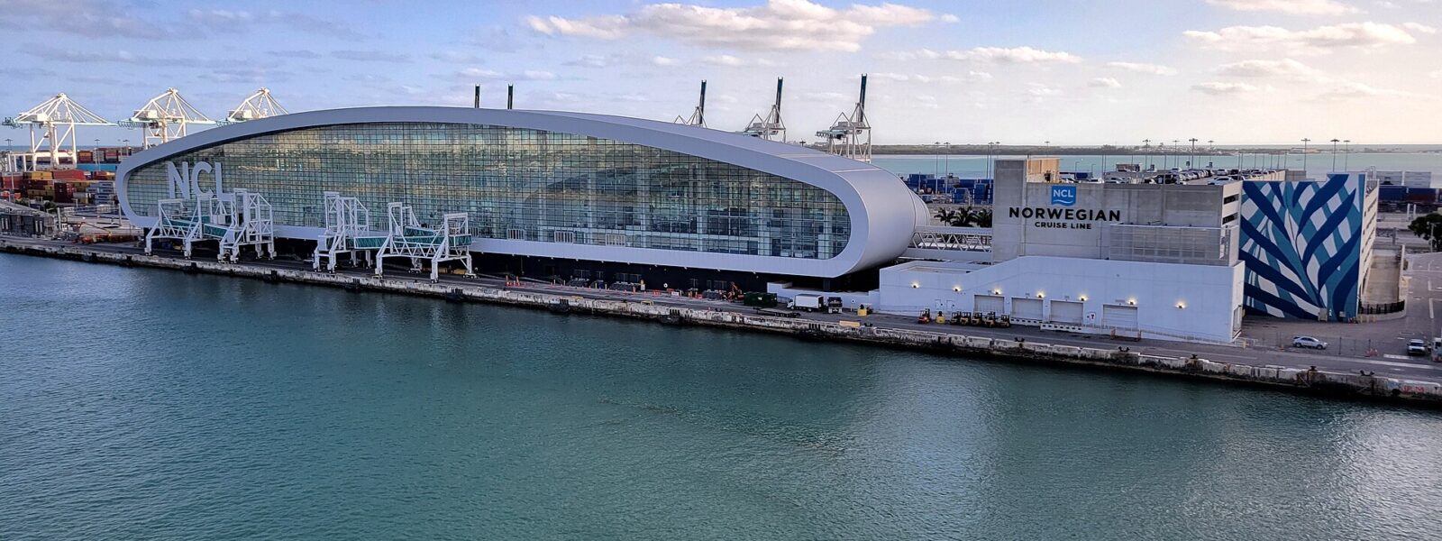 The elliptical glass Norwegian Cruise Line Terminal B at PortMiami with three boarding bridges alongside