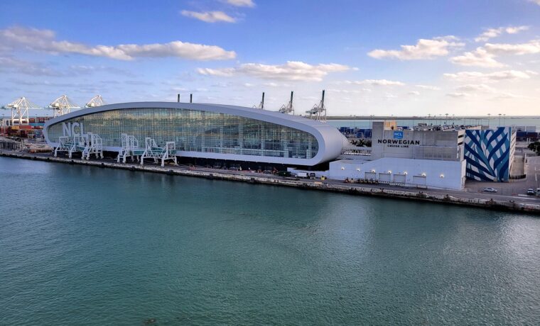 The elliptical glass Norwegian Cruise Line Terminal B at PortMiami with three boarding bridges alongside