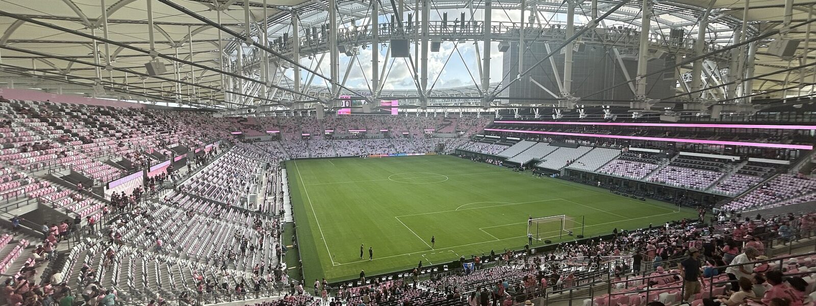 Fans in pink and black Messi number 10 shirts taking their seats in the upper level of Nu Stadium beneath the white canopy roof