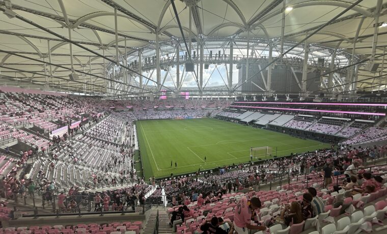 Fans in pink and black Messi number 10 shirts taking their seats in the upper level of Nu Stadium beneath the white canopy roof