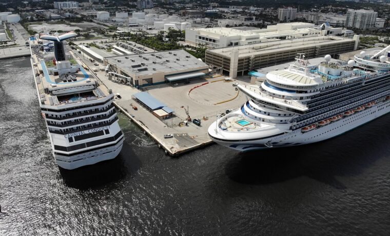 Aerial view of two cruise ships berthed at a Port Everglades terminal, with a parking garage and the Fort Lauderdale skyline behind