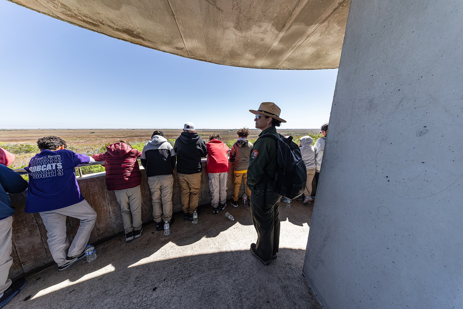 A park ranger and a group of visitors in jackets looking out over the sawgrass from the Shark Valley observation tower