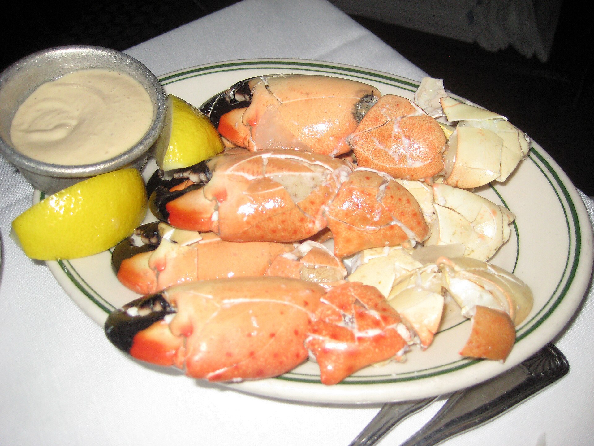 A plate of cracked stone crab claws with lemon wedges and mustard sauce