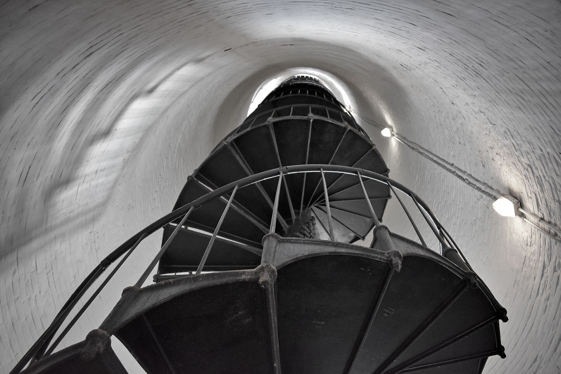 Looking straight up a black cast-iron spiral staircase winding inside the whitewashed brick tower of the Cape Florida Lighthouse