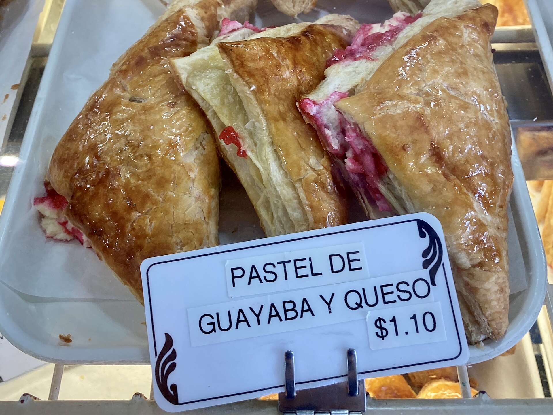 Guava-and-cheese pastelitos in a Miami bakery display, with glossy pastry crusts and a Spanish label in front.