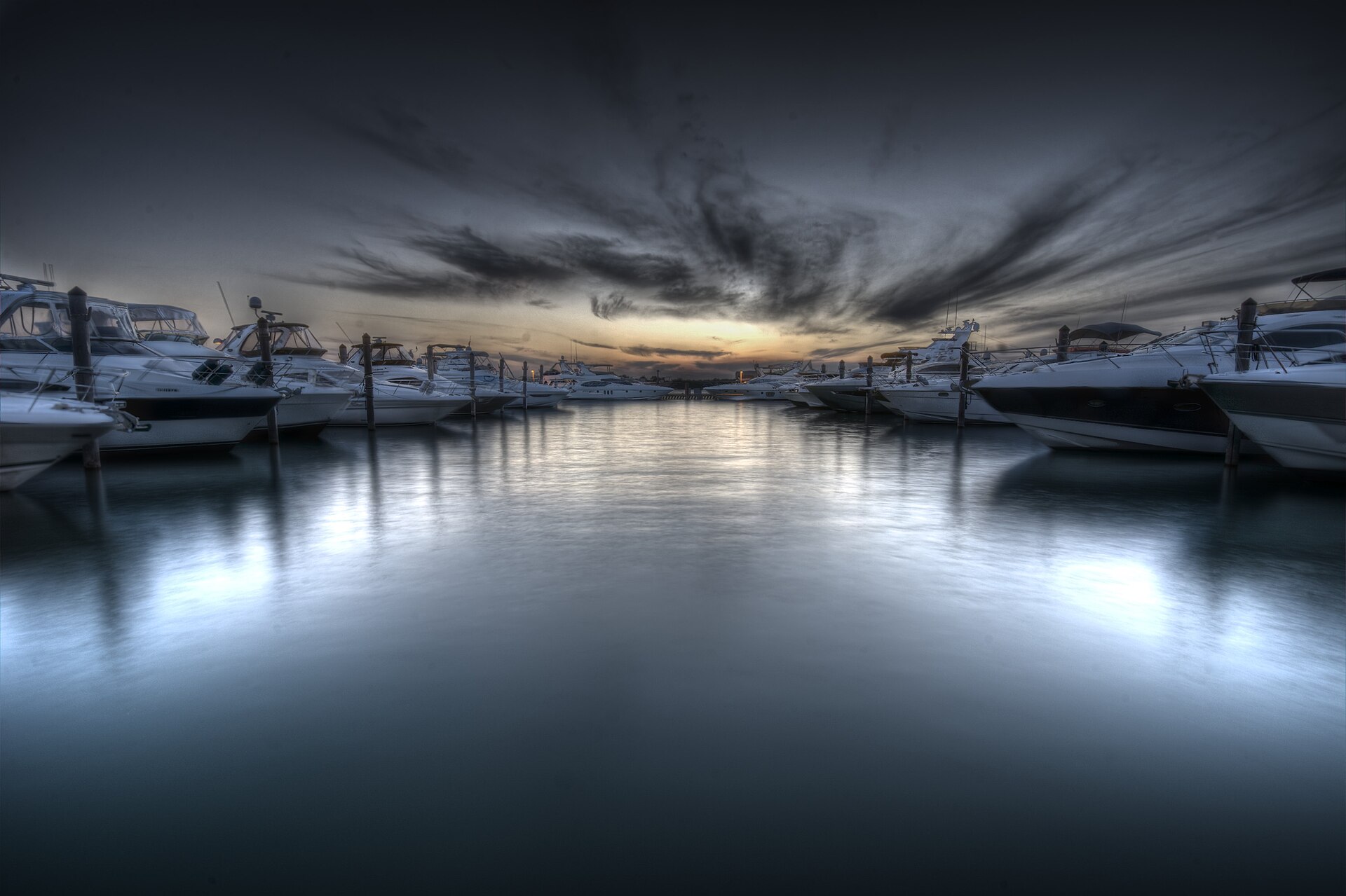 Rows of white motor yachts moored on either side of still water at the Haulover Park marina under a streaked evening sky