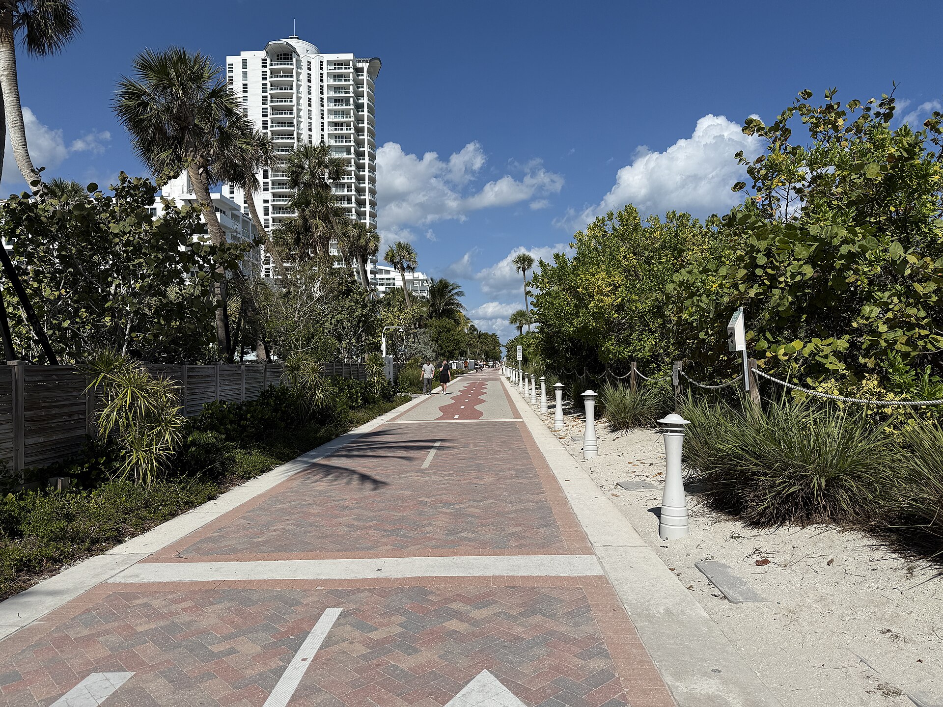 The Miami Beach Beachwalk stretches north at 40th Street between waterfront buildings, palms, and dense dune vegetation.