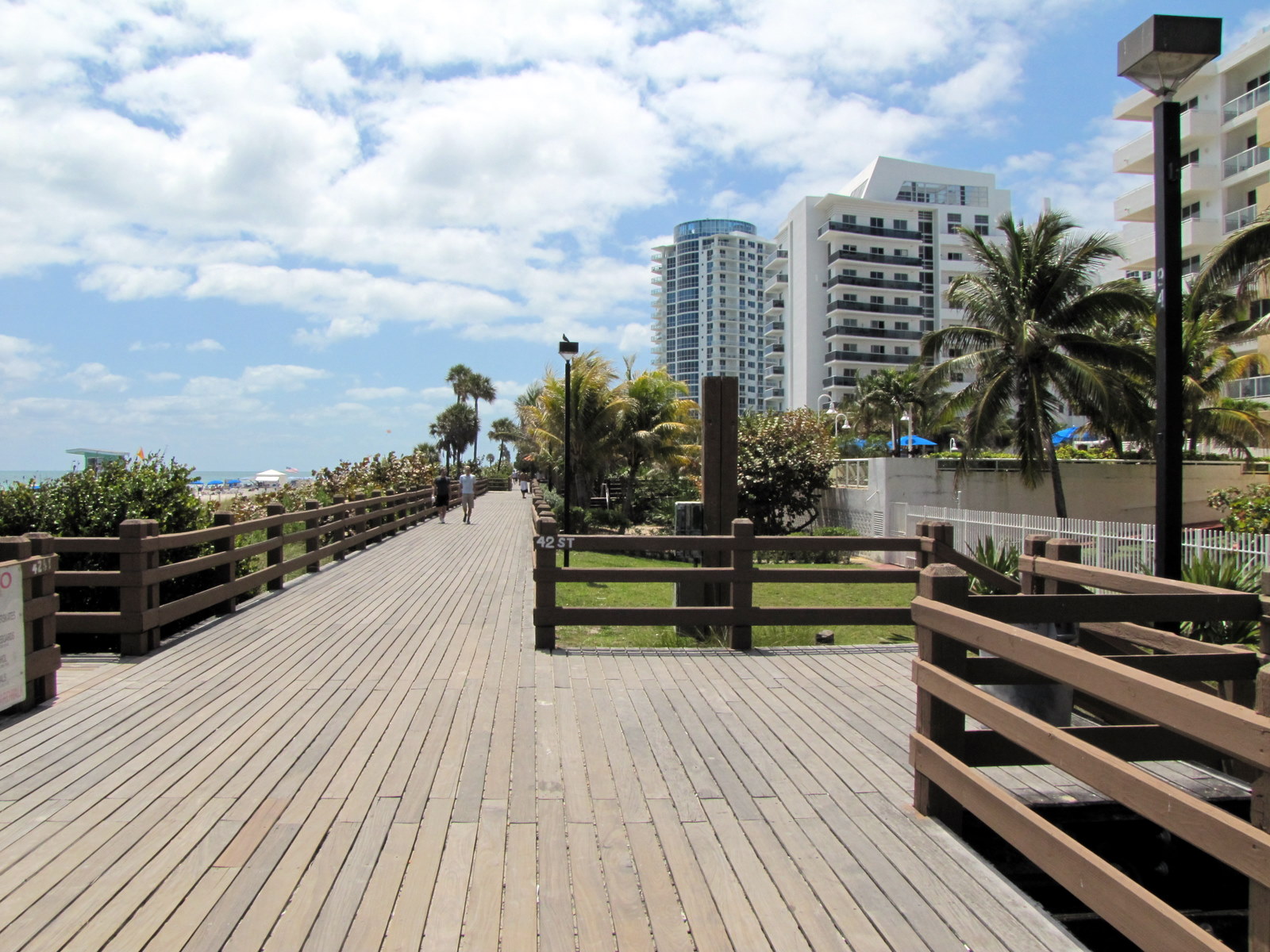 The old wooden boardwalk in Mid-Beach at 42nd Street, with brown wooden railings, sea grape on the dunes, a lifeguard stand on the beach and condo towers to the right