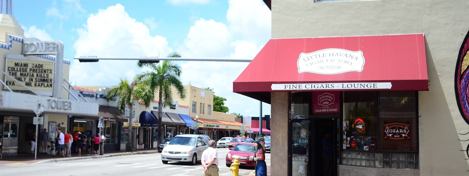 Pedestrians pass a red-awning cigar shop on Calle Ocho in Little Havana, with the Tower Theater across the street.