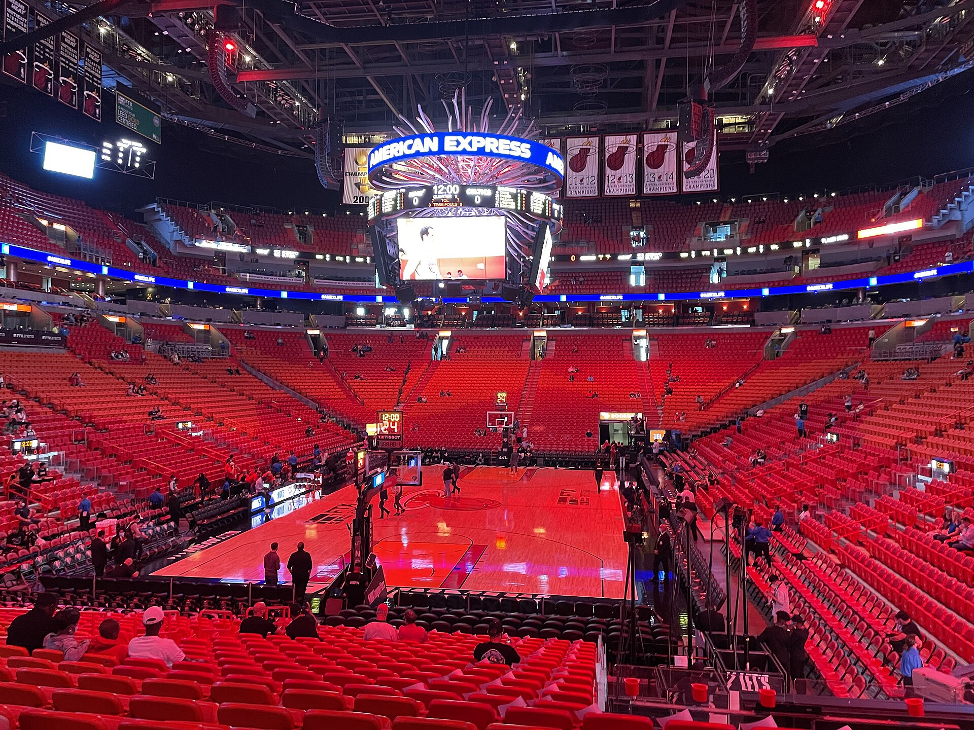Red seats surround the Miami Heat basketball court inside the Kaseya Center, with a large scoreboard suspended overhead.