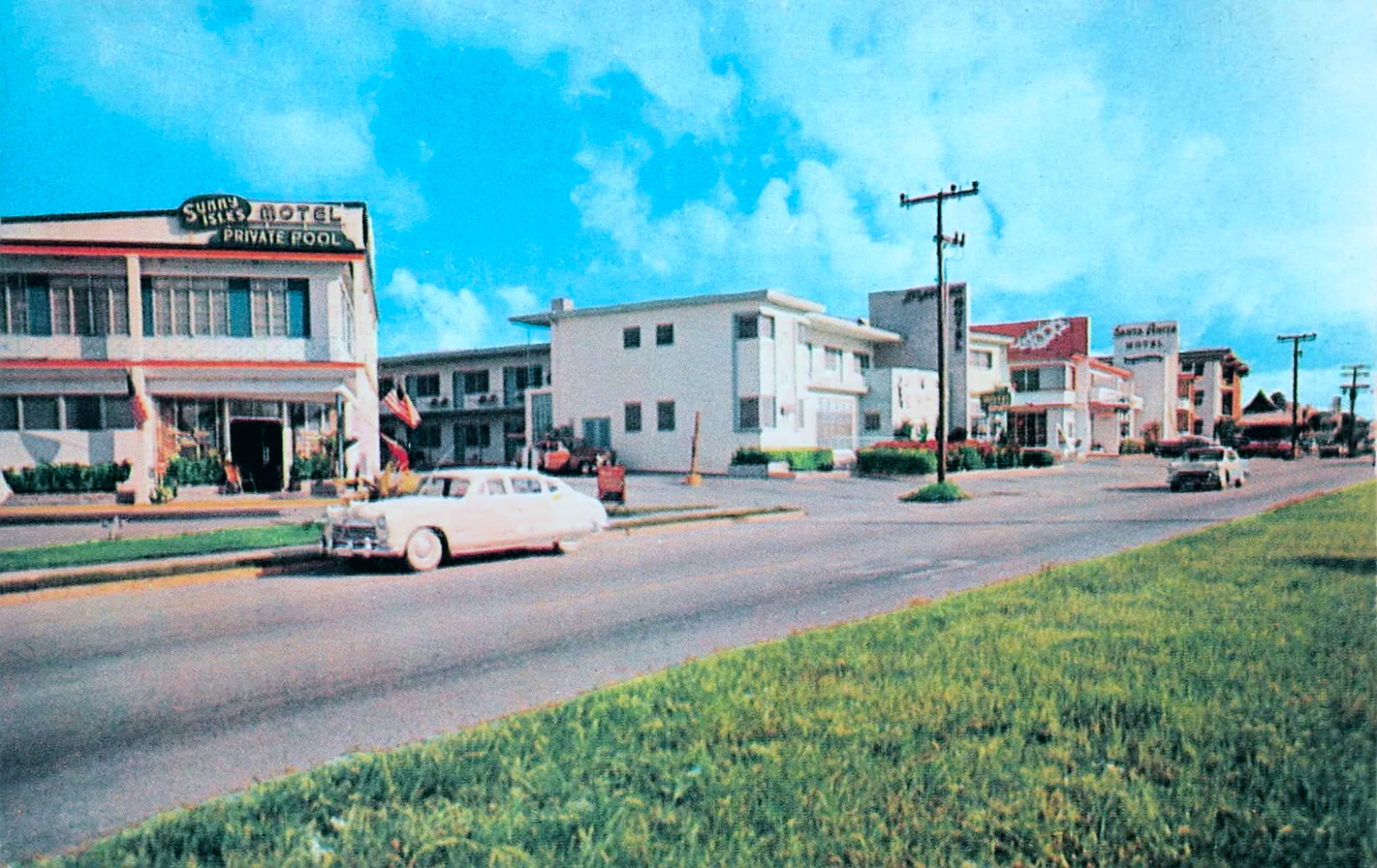 A colorized vintage postcard of Collins Avenue at Sunny Isles lined with low motels, including the Sunny Isles Motel with a private pool sign, a 1950s car parked in front