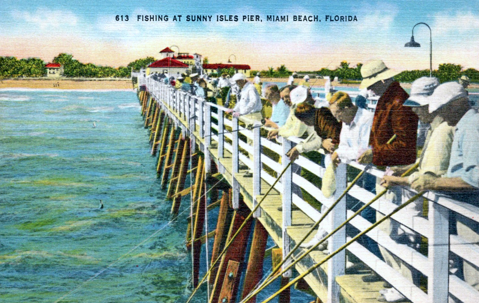 A colorized vintage postcard of men in hats fishing from the railing of a long wooden pier at Sunny Isles, with a red-roofed pavilion and palms on the shore